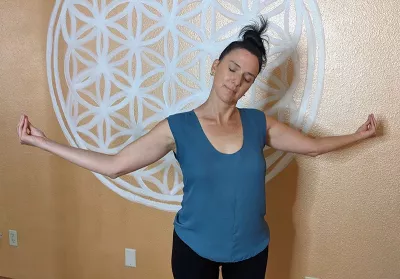 nicole Reed performing a crane's beak neck stretch in the shoulders with her arms outstretched.