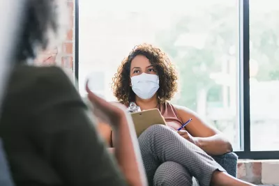 A woman wearing a face mask while doing an intake with a client.