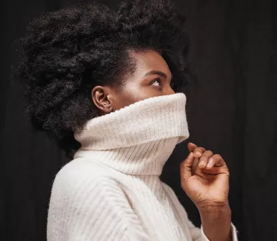 Black woman with a large knitted sweater pulled up over her face. 
