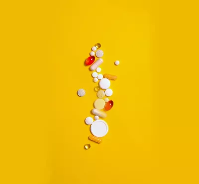 different-shaped pills, tablets, and capsules all scattered across a yellow background.