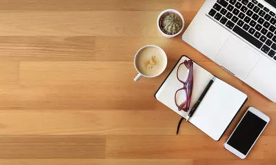 a cup of coffee, pair of glasses, notebook and computer on a table.