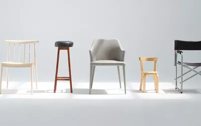 A row of different kinds of chairs and stools lined up in an empty room.