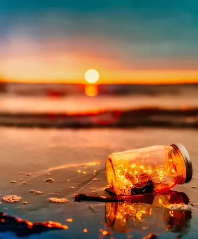 yellow string lights in a jar, floating on a beach at sunset.
