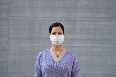 a woman in a purple sweater wears a disposable face mask.
