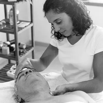 A female massage therapist touches a client's forehead and neck.