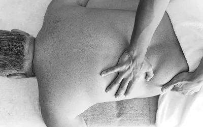 A prone client has his back and side worked on by a massage therapist.