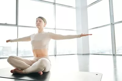 a woman seated criss-cross with her arms outstretched in a yoga pose.