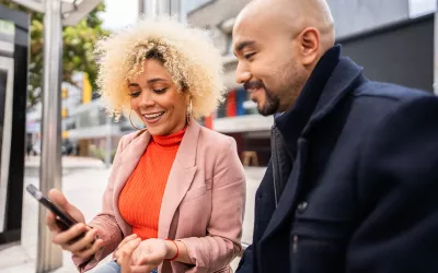 A woman shows a man her cell phone while standing outside.