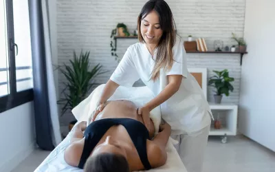 A massage therapist massages a pregnant woman on a table.