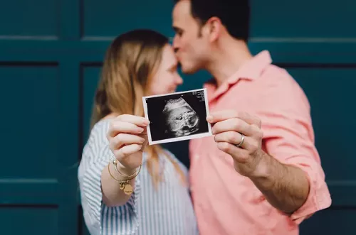 a male and female couple kiss while they hold up an ultrasound photo of a baby.