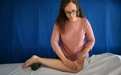 A massage therapist works on the back of a leg of a prone client.