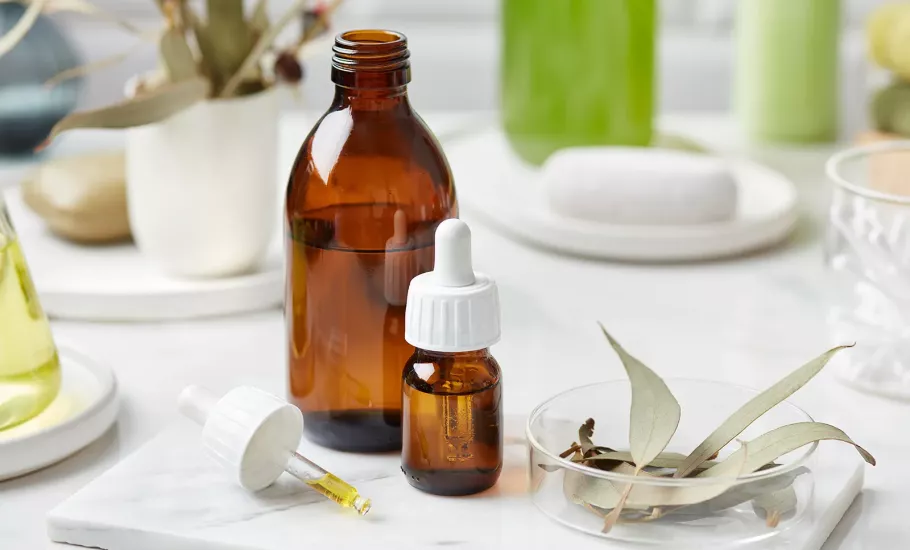 a bottle of essential oil, a dropper, a cup, and a bundle of sage on a table.