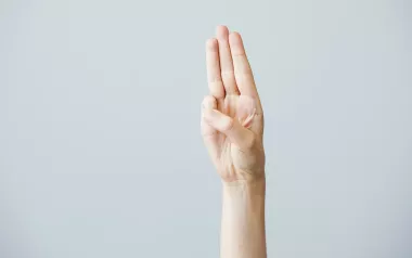 A hand displays the middle three fingers in a Scout's Honor pose with thumb and pinky finger touching.