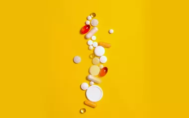 different-shaped pills, tablets, and capsules all scattered across a yellow background.