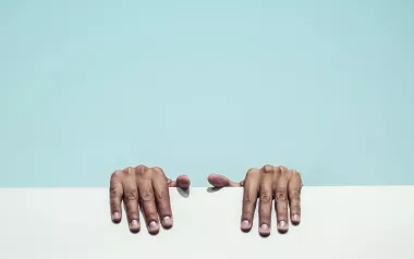 two hands grip a white ledge behind a blue background. 