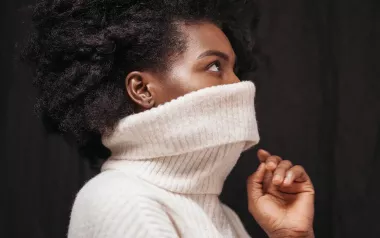 Black woman with a large knitted sweater pulled up over her face. 