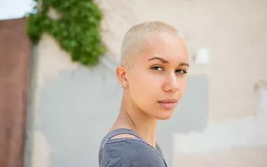 woman with bleached hair and buzzcut looks seriously towards the camera.