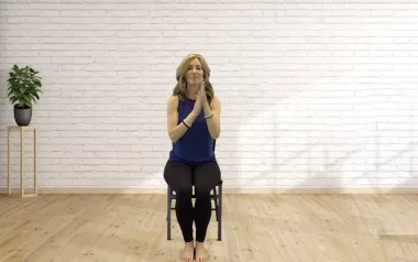 Author Angie Parris holds her hands at heart center while sitting in a chair. 