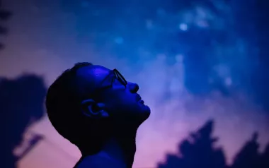 A man gaves up into the starry night sky with his head tilted backward.