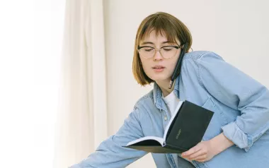 young woman talking on the phone and opening a notebook at the same time.