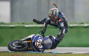 A motorcycle racer lays the bike over too far and is in midair after jumping off it.