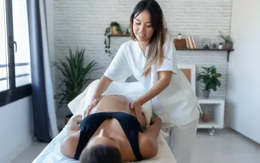 A massage therapist massages a pregnant woman on a table.