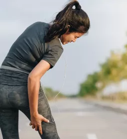 A woman grabs the back of her right leg which is causing her pain.