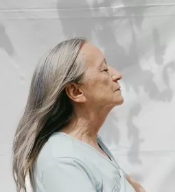 An elderly woman stands with her face to the breeze.
