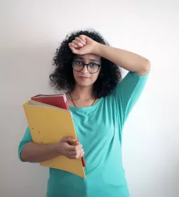 Woman looking distressed holding one arm to her forehead and using the other arm to hold a folder and binder