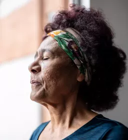 mature woman standing near a window with eyes closed breathing in.