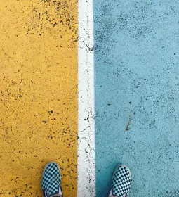 Conceptual, feet standing on divided road, half blue, half yellow.