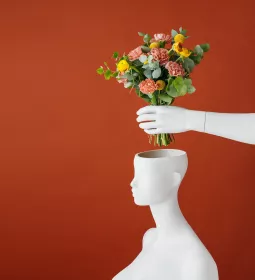 a bouquet of red and yellow flowers is placed into a vase shaped like a head.