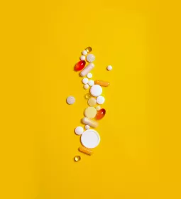 different-shaped pills, tablets, and capsules all scattered across a yellow background.
