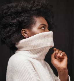 Black woman with a large knitted sweater pulled up over her face.