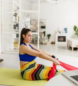 a woman on a yoga mat uses a stretching band on her feet as she follows an online class.