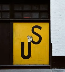 Grafitti art on an orange wall with the letters U and S spelling Us, holding hands.