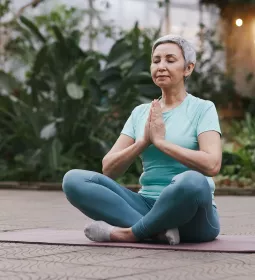 older woman with short hair seated criss-cross on a mat with her hands at heart center.