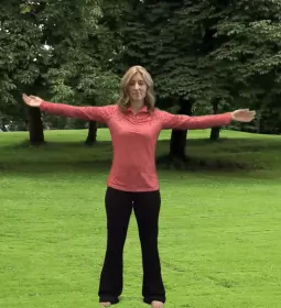 author Angie Parris stands outside on the grass, stretching with her legs and arms outstretched.