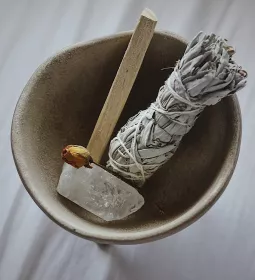 a smudge stick, wood, and a quartz crystal in a bowl.