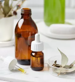 a bottle of essential oil, a dropper, a cup, and a bundle of sage on a table.