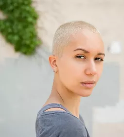 woman with bleached hair and buzzcut looks seriously towards the camera.