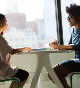 two women seated at a table across from each other, talking.