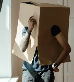 A person wearing a moving box over their head ponders change.