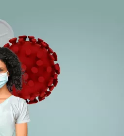 A woman with curly long hair wearing a face mask stands in front of a cartoon red cell.