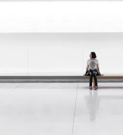 a woman sits on a long bench in an empty room.