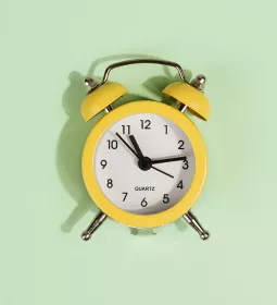 an analog alarm clock against a pale mint-green background.