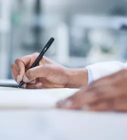 a person's hands use a black pen to write on a sheet of paper.