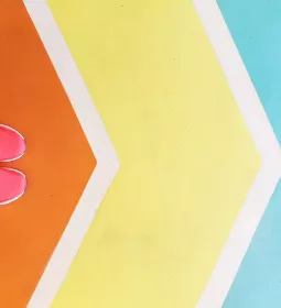 A pair of feet in pink sneakers stand on a colored path of chevron arrows.