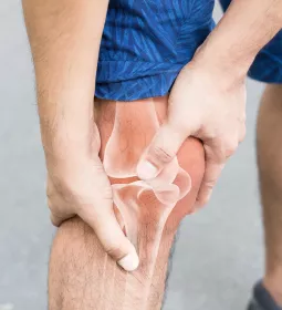 Person in shorts clutching their knee with a see-through overlay of the leg bones and joints underneath.