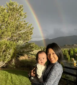 Kei Yumoto and child standing outside with a rainbow in the background.